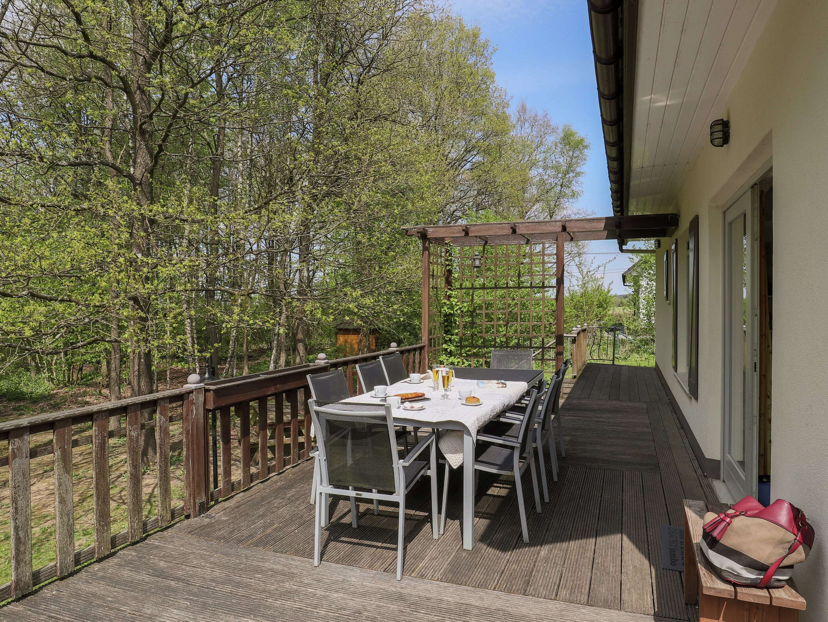 An outdoor dining area with a table and chairs, a pergola, and a view of trees.