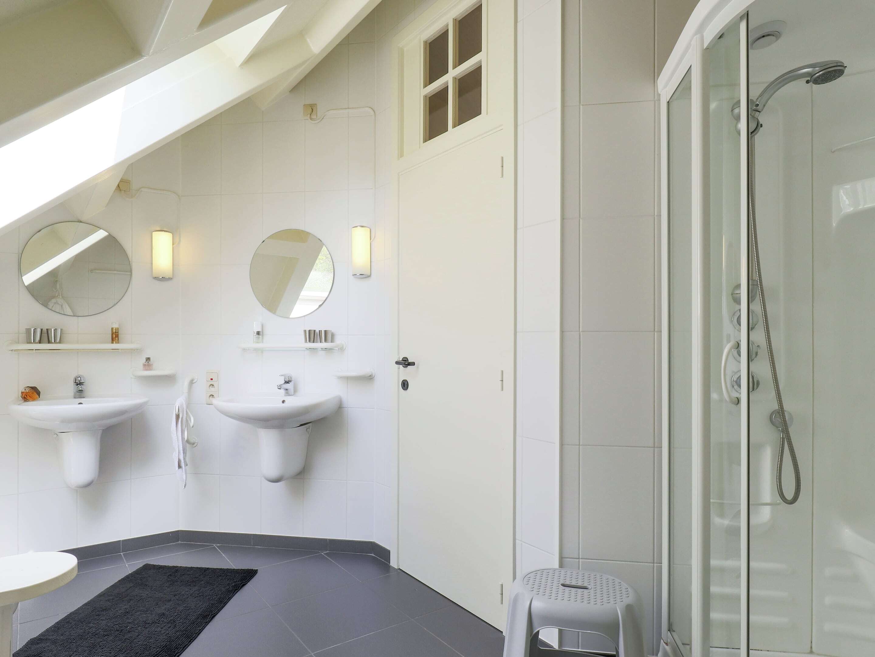 A modern bathroom with two sinks, a glass shower enclosure, and a small stool.