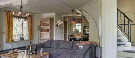 A living room with a sectional sofa, a glass coffee table, a chandelier, and a view into the kitchen.