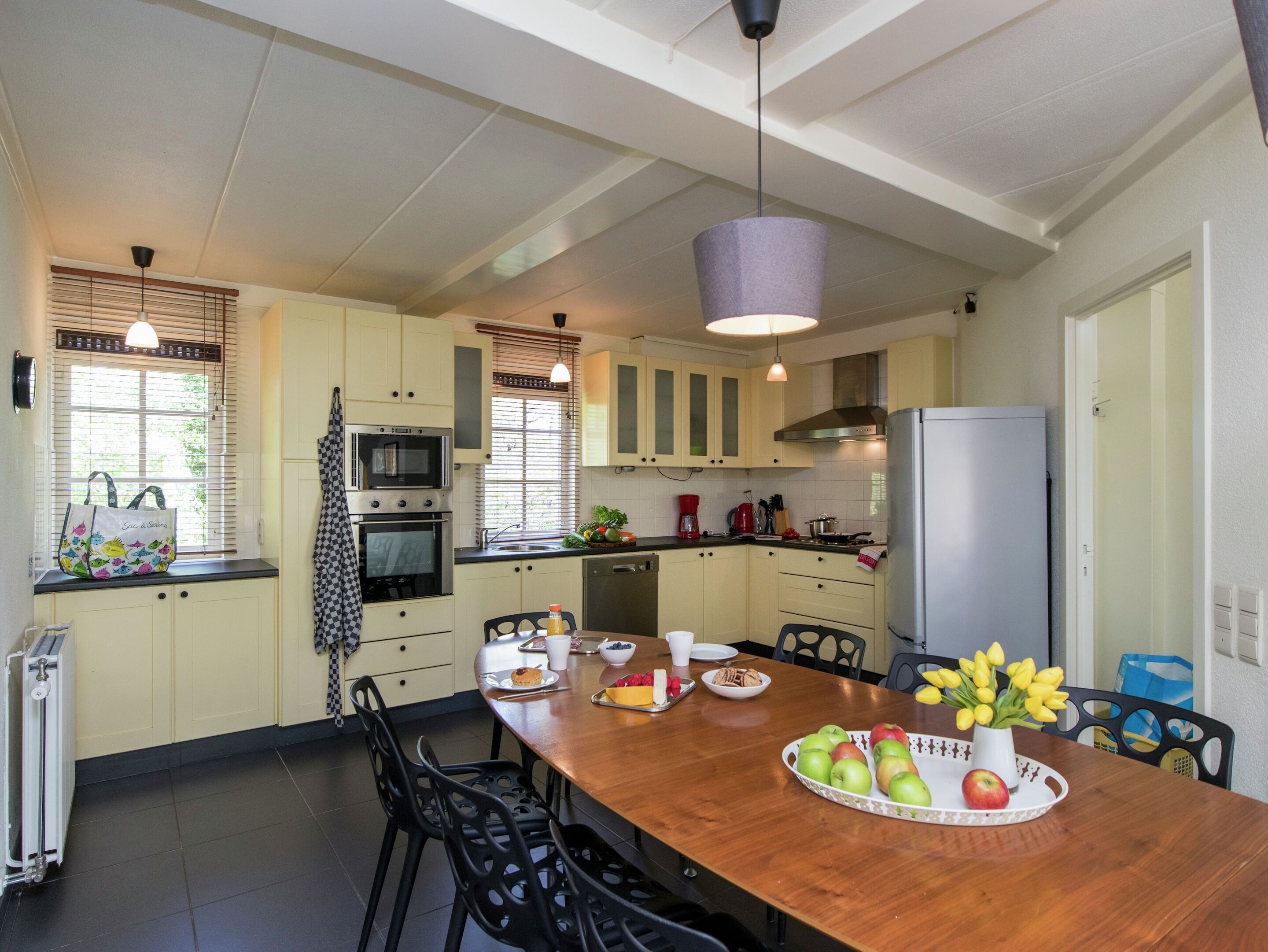A kitchen with a wooden table, chairs, a refrigerator, and a microwave.