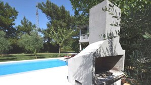 Ein Pool mit Betonstruktur und überdachter Grillgegend.
