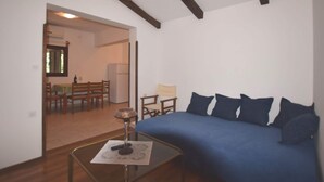 Ein Zimmer mit einem blauen Sofa, Holzboden und einem Essbereich, der durch einen offenen Durchgang sichtbar ist.