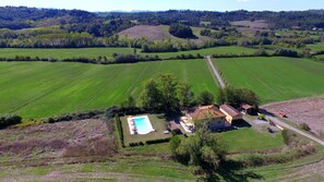 An aerial view of a rural property with a swimming pool, a small building, and surrounding fields.