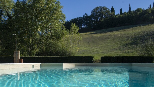 A swimming pool with clear water, surrounded by a grassy area and trees. - Villa in Tuscany Near Medieval Ghizzano (Peccioli)