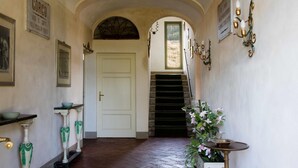 A hallway with a white door, a staircase, and wall-mounted sconces. - Villa in Tuscany Near Medieval Ghizzano (Peccioli)