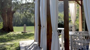 A covered outdoor seating area with white curtains, stone flooring, and a tree in the background. - Villa in Tuscany Near Medieval Ghizzano (Peccioli)