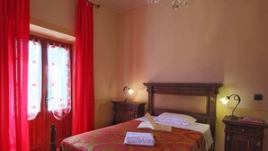 Ein Schlafzimmer mit einem großen Bett, zwei Nachttischen mit Lampen, einem Holzkopfstück und roten Vorhängen.
