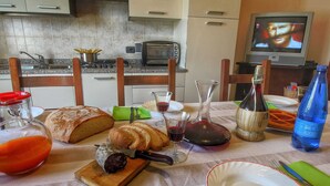 Ein Esstisch gedeckt mit Brot, Wein und einer Flasche, in einer Küche mit Fernseher und Schränken.