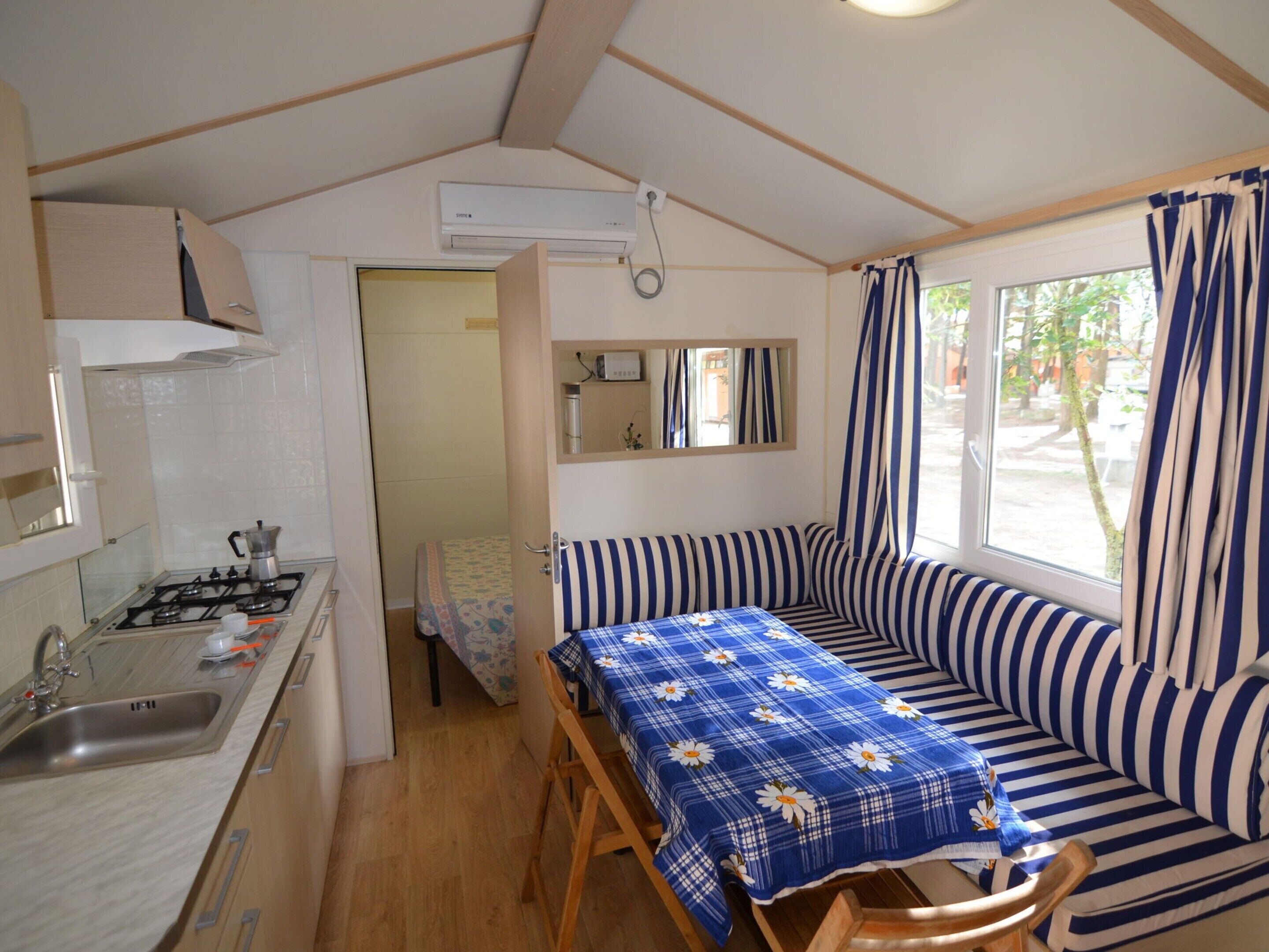 A compact kitchenette with a gas stove, sink, and a small dining table with a blue floral tablecloth.