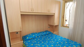 Ein kleines Schlafzimmer mit einem Einzelbett, Holzschränken und einem Fenster mit Vorhängen.