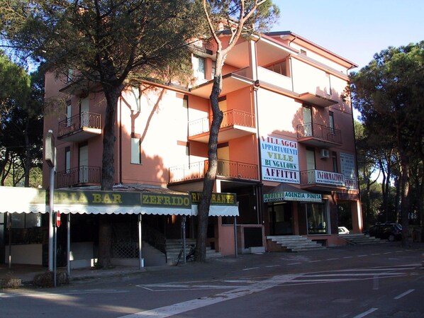 Stylish building with a pink facade, featuring balconies on each floor and a storefront with a bar and restaurant below.