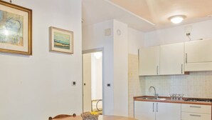 A kitchen with white cabinets, a sink, and a stove. There is a dining table with chairs and a basket of fruit.