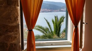 A window with orange curtains, a view of a lake, and a palm tree. - Coastal Apartment in Vis Near sea (Vis)