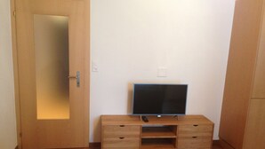 A room with a wooden cabinet, a television on a stand, a door, and a light switch on the wall. - Spacious Apartment in Riederalp near Ski Trail (Riederalp)