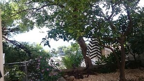 A garden area with potted plants, a stone wall, and a tree with a black and white striped item hanging from it. - Delightfully Decorated Apartment with Sea View near Beach (Brela)