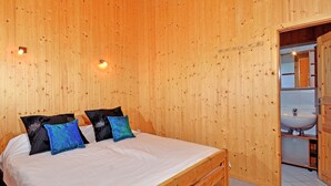 Dormitorio con paneles de madera, cama, almohadas y baño visible con lavamanos.