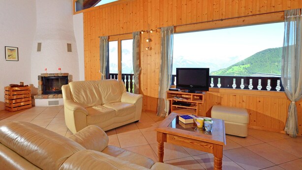 Una sala de estar acogedora con chimenea, un sofá, un televisor y un balcón con vistas a la montaña.