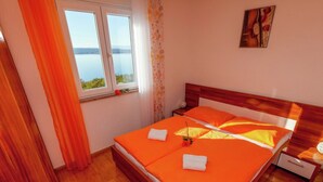 A double bed with orange bedding, a wooden headboard, a nightstand, and a window with a view of a body of water. - Country House in Croatia With Pool (Crikvenica)