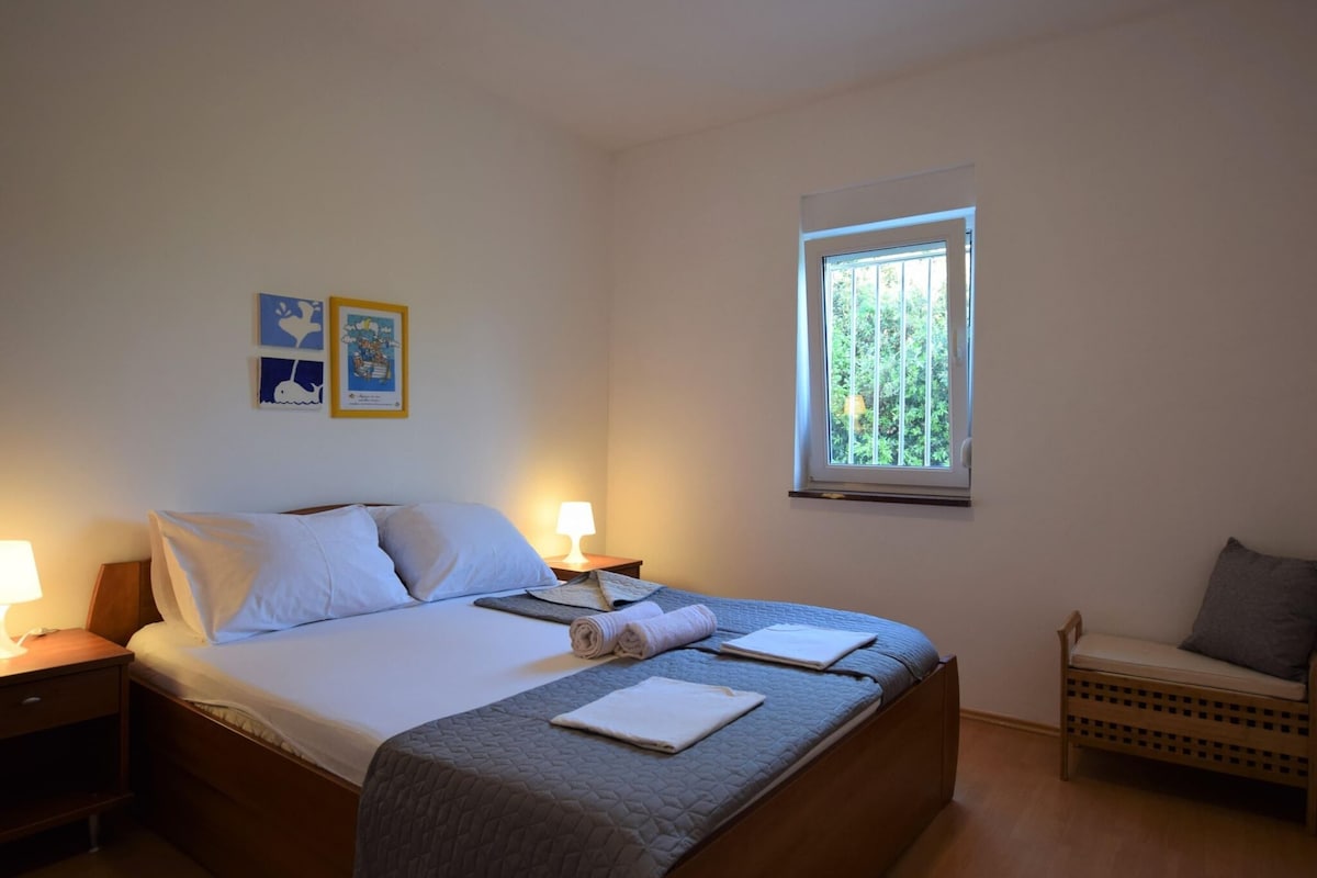 Quarto com cama, luminárias de cabeceira, janela e uma cadeira.