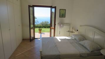 A bedroom with a bed, a nightstand, a window, and a view of the outdoors.