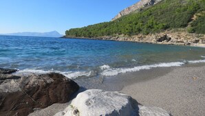Uma praia com águas azuis cristalinas, costa rochosa e montanhas ao fundo.