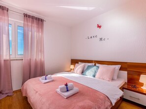 A bedroom with a bed, pillows, a nightstand, a wall decoration, and a window with curtains.