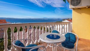 A balcony with a white balustrade, a round table with two chairs, and a view of the sea and distant mountains. - Gorgeous Apartment With Hot Tub and Terrace With Sea View (Crikvenica)
