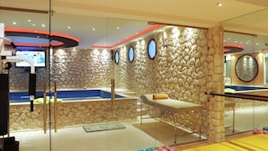 Un espace spa moderne doté d’un mur en pierre, d’une table de massage, d’un jacuzzi et d’appareils d’exercice.