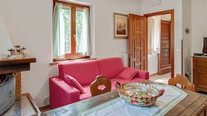Uma sala de estar aconchegante com um sofá vermelho, uma mesa de madeira com uma tigela decorativa e uma janela com cortinas.