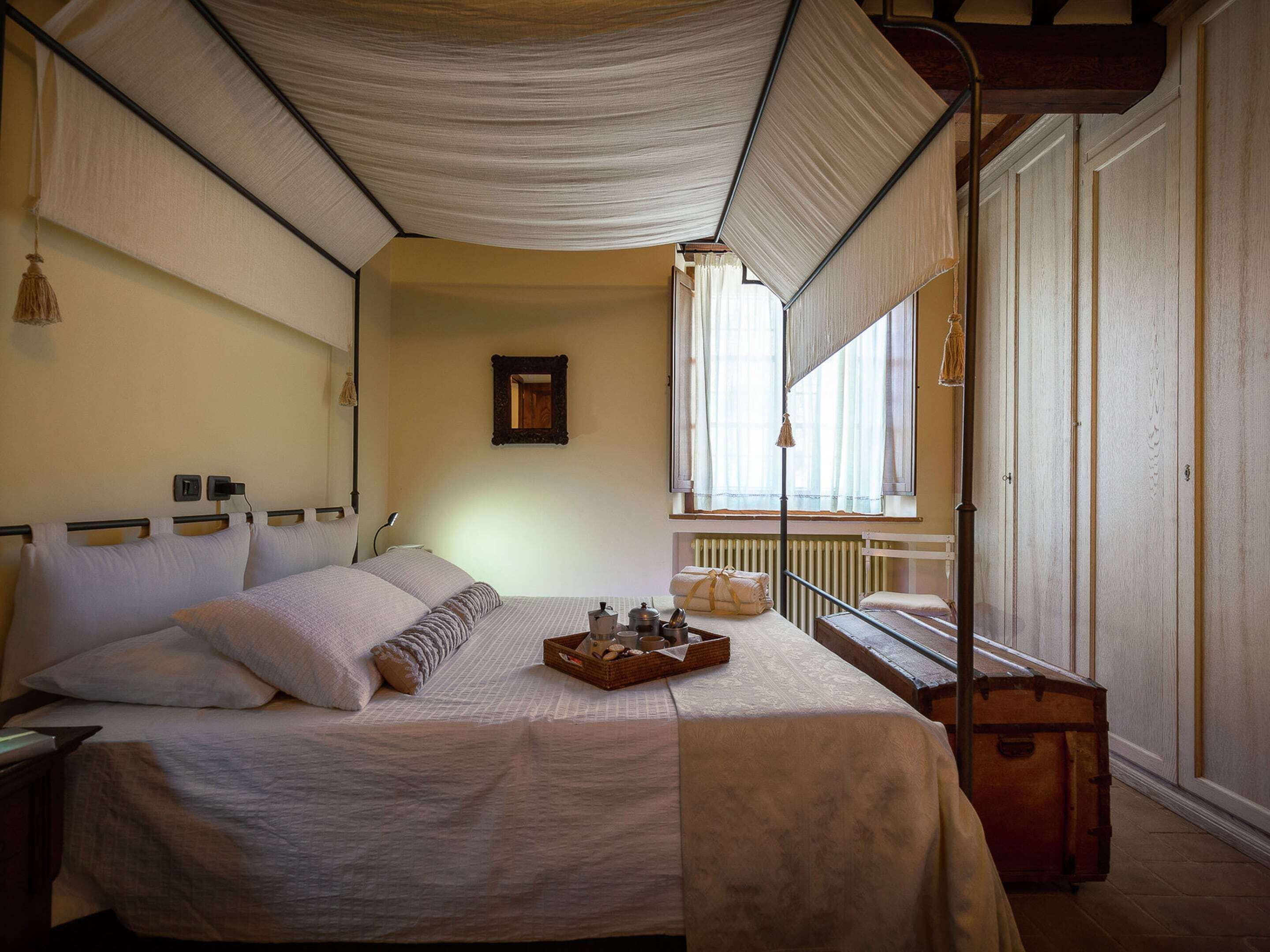 Een slaapkamer met een bed, nachtkastje, lamp, raam en een koffer.