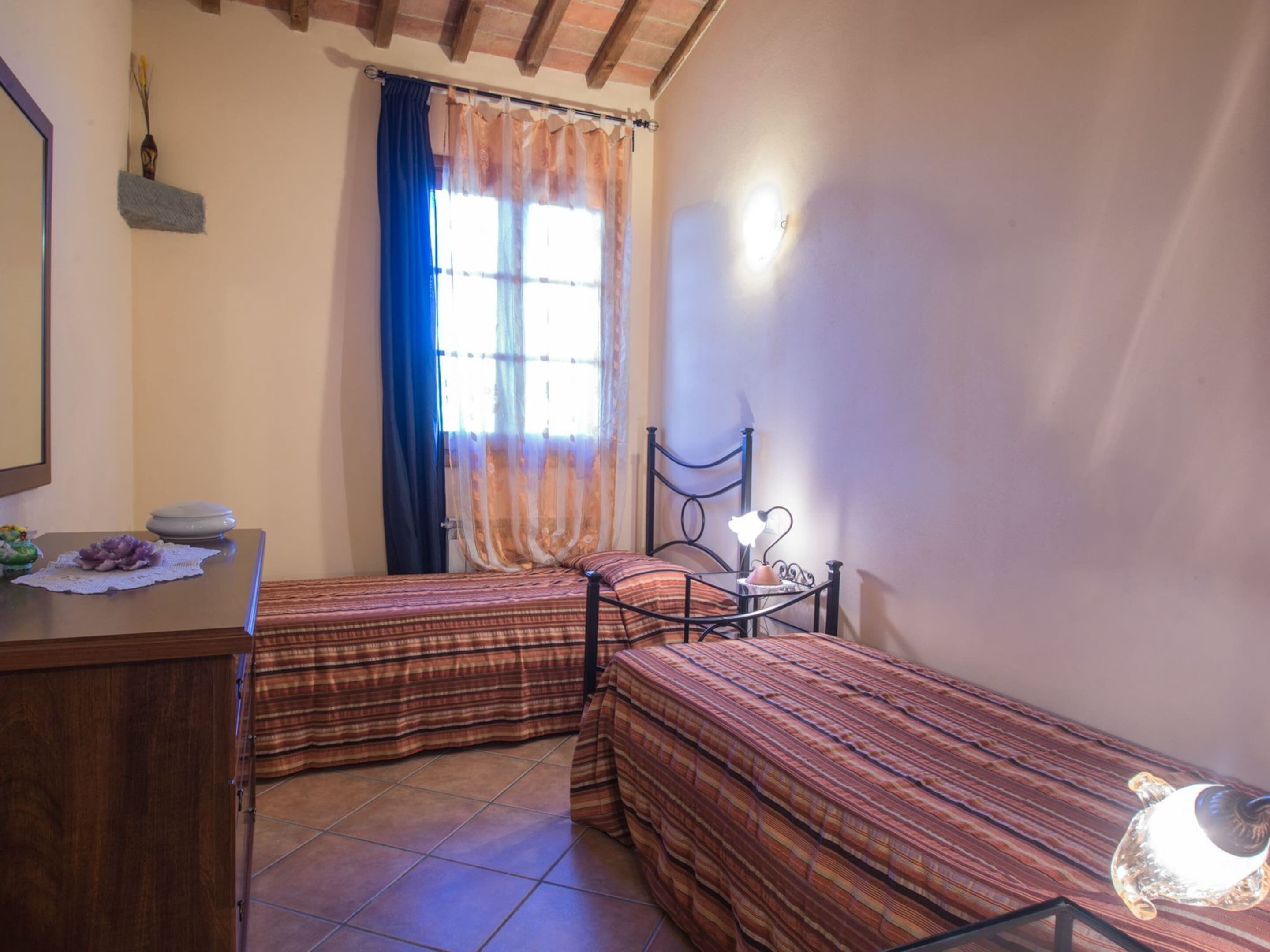 A bedroom with two beds, a wooden dresser, a nightstand, and a window with curtains.