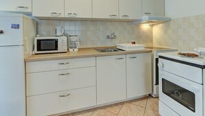 A compact kitchen with white cabinets, a microwave, a coffee maker, a sink, and a stove. - Apartment in Senj With Sea Views & BBQ (Senj)