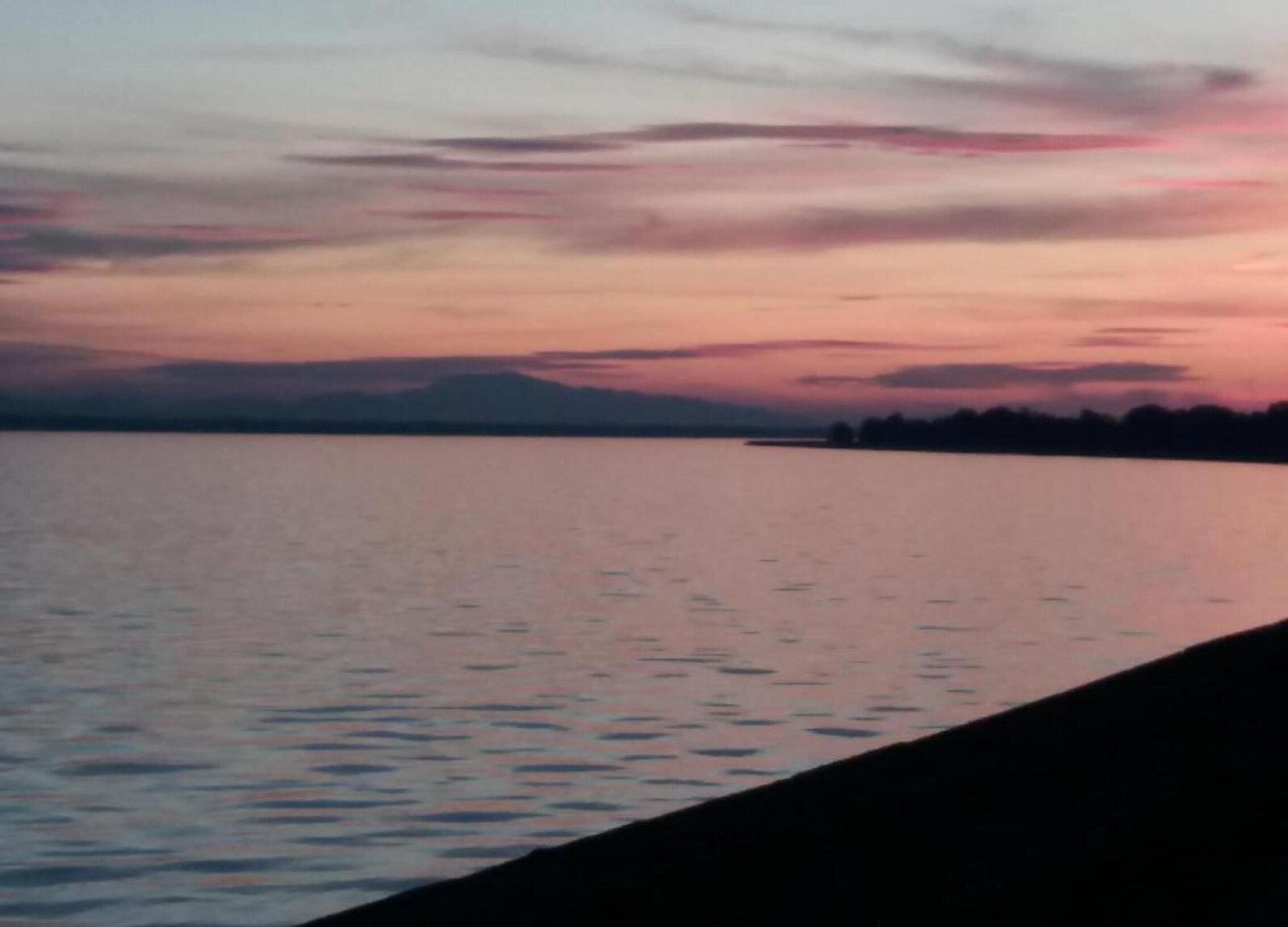 Un coucher de soleil sur une étendue d'eau calme, avec une chaîne de montagnes en arrière-plan.