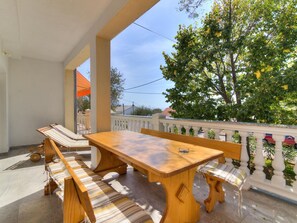 Une table et des bancs en bois sur un balcon extérieur, avec vue sur les arbres et les bâtiments.