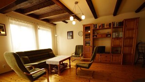 A cozy living room with a wooden floor, a sofa, two armchairs, a coffee table, and a bookshelf filled with books.