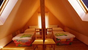 A cozy attic bedroom with two beds, a wooden chair, and a sloped ceiling.