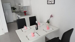 Eine moderne Küche mit weißen Schränken, einem Esstisch gedeckt mit rosa Servietten und Weingläsern, und einer Topfpflanze auf der Arbeitsfläche.
