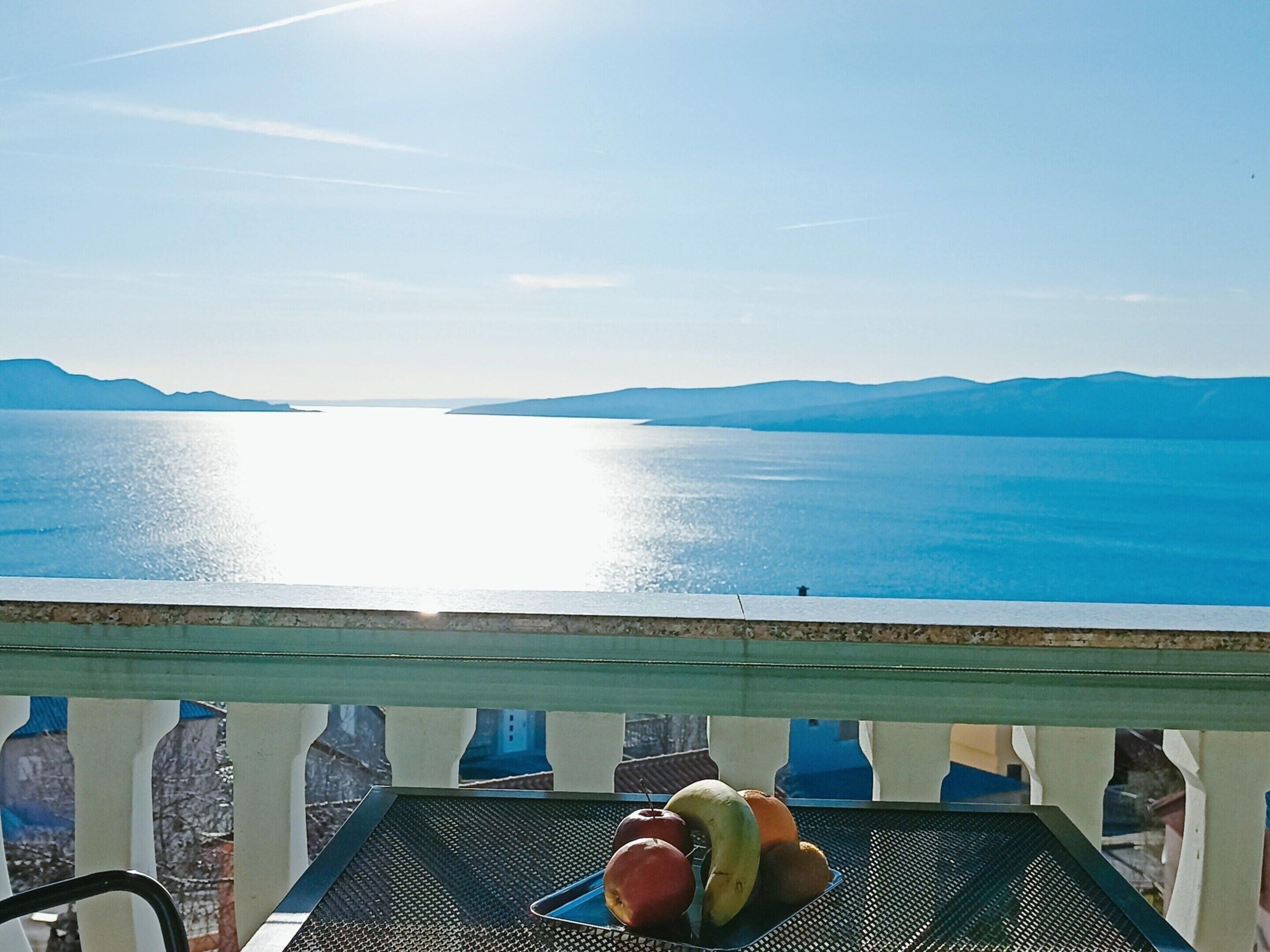 Un balcon offrant une vue sur une mer calme et des montagnes lointaines.