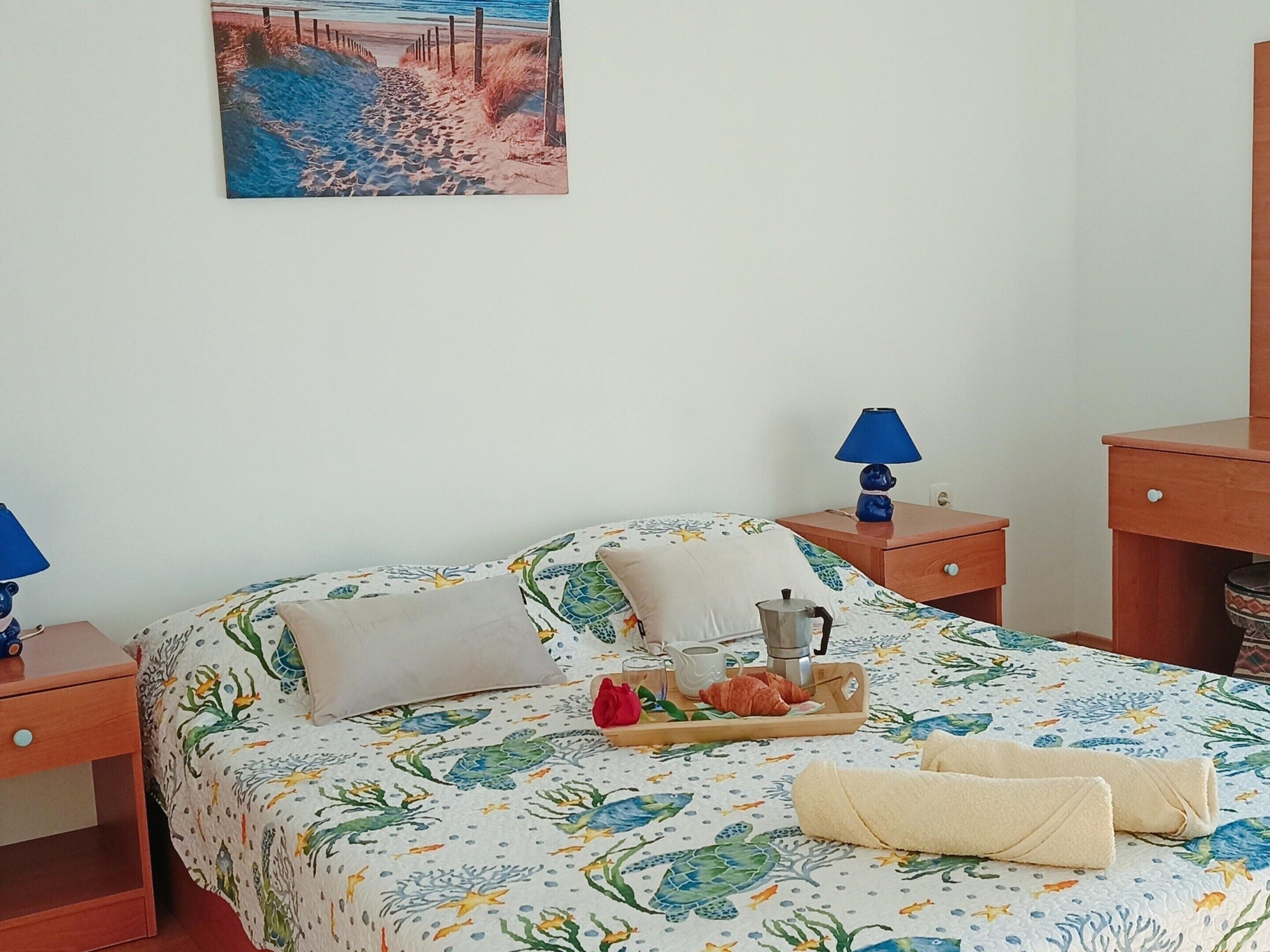 A neatly made bed with a floral bedspread, a bedside table with a lamp, and a tray with breakfast items.