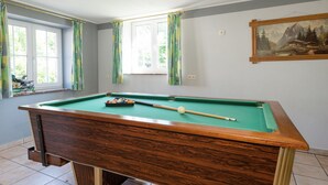 Una mesa de billar en una habitación con dos ventanas y un cuadro en la pared.