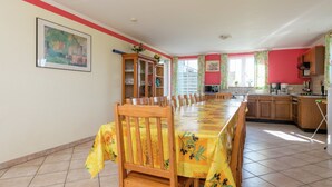 Un comedor con una mesa larga, sillas y una cocina al fondo.