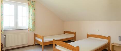 A room with two wooden beds, a radiator, a window with floral curtains, and a small bedside table.