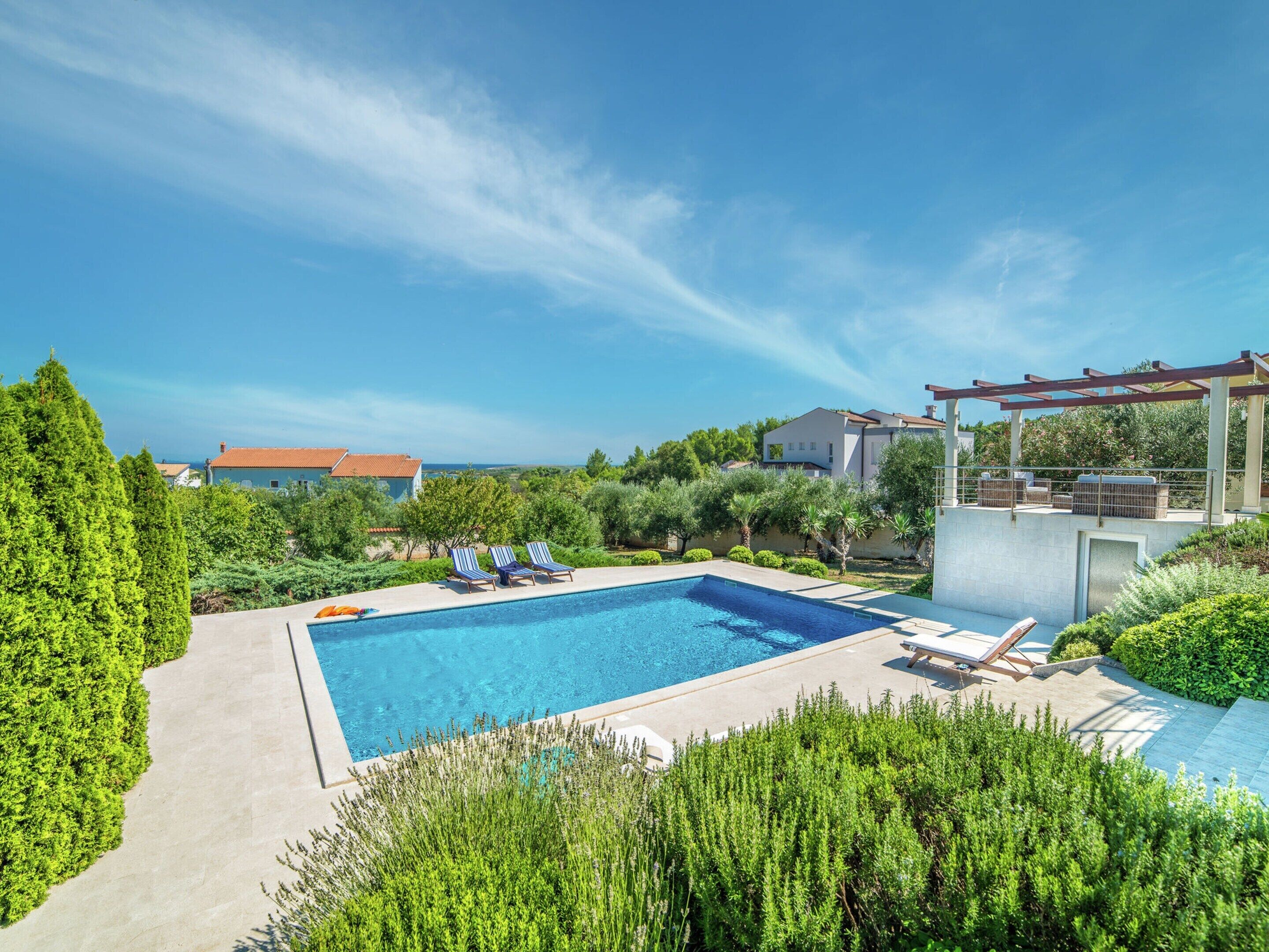 Una piscina con sillas de descanso, rodeada de vegetación y casas.