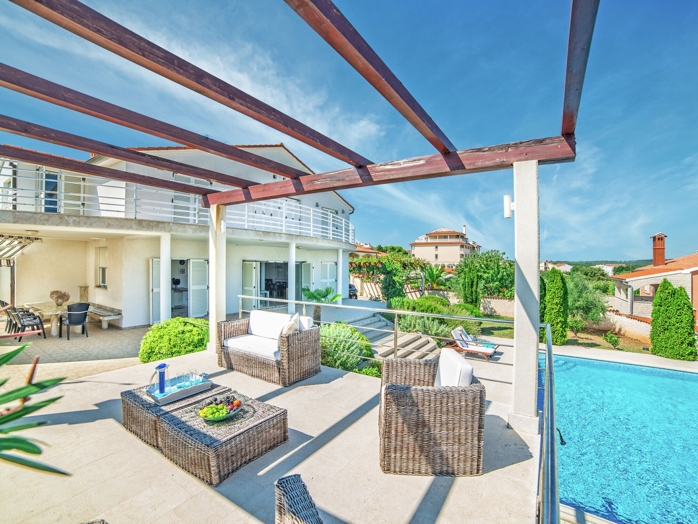 A covered outdoor area with wicker furniture, a pool, and a view of surrounding buildings.