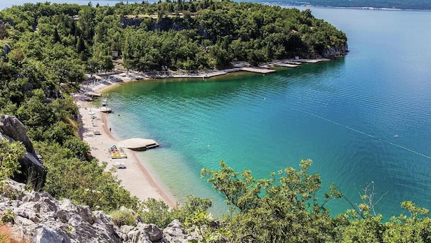 Uma área costeira com praia, águas turquesa cristalinas e uma península arborizada.