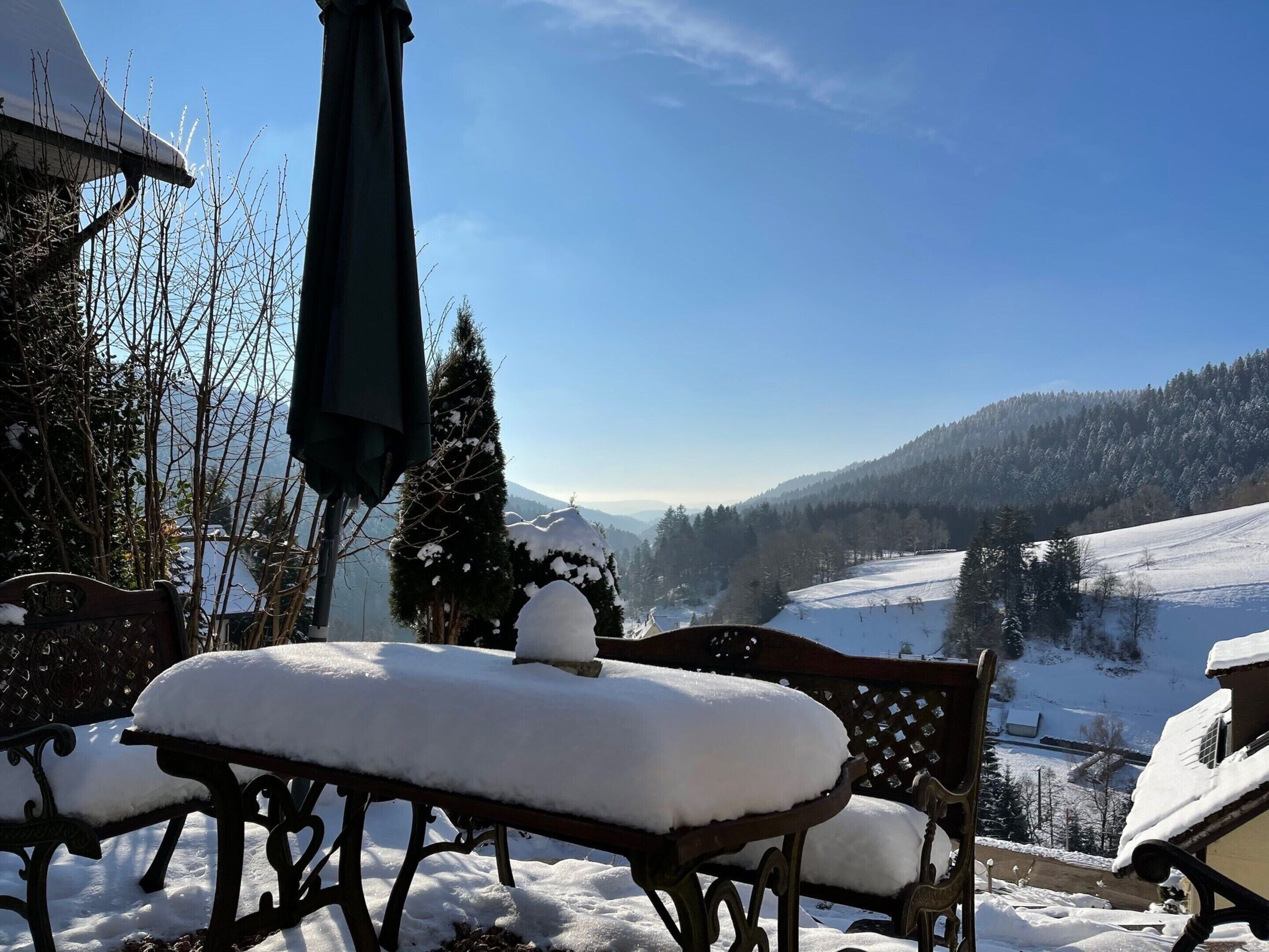 Ein mit Schnee bedeckter Außenbereich mit Sitzgelegenheiten und Blick auf eine verschneite Berglandschaft.