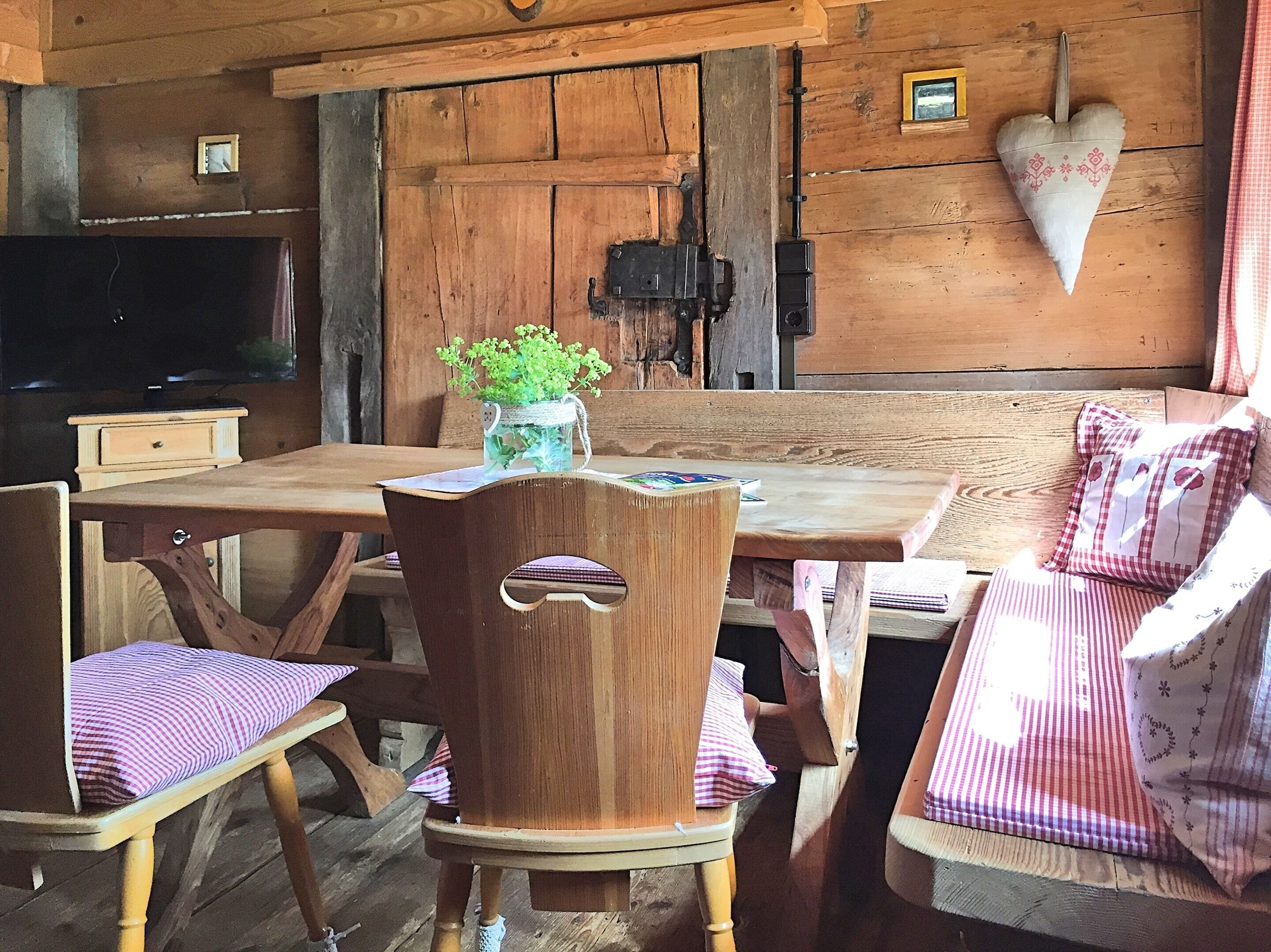 A rustic wooden cabin interior with a wooden dining table, chairs, and a bench.
