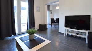 A modern living room with a flat-screen TV, a potted plant, and a dining area in the background. - Spacious and Modern Apartment on the Beach in Klek (Slivno)