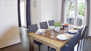 A dining area with a wooden table set for four, surrounded by chairs, with a view of greenery outside. - Spacious and Modern Apartment on the Beach in Klek (Slivno)