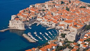 An aerial view of a historic coastal city with a fortified castle, a harbor with numerous boats, and buildings with red-tiled roofs. - Spacious and Modern Apartment on the Beach in Klek (Slivno)